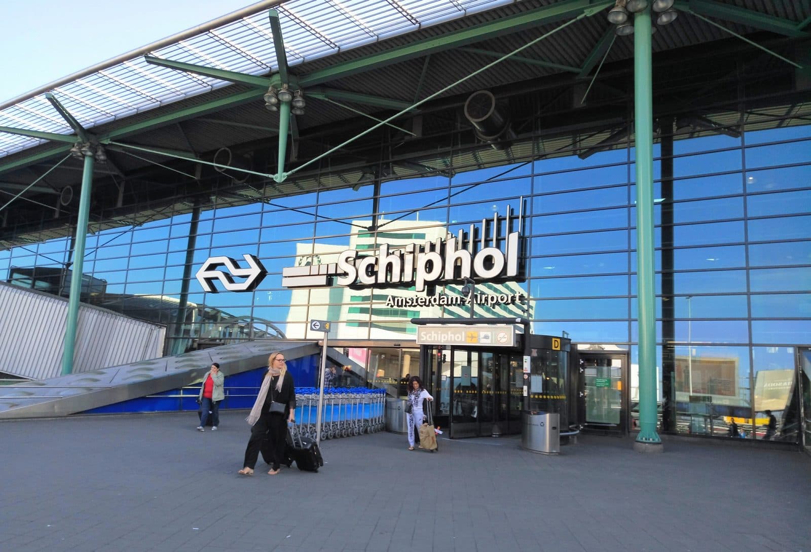 Reizigers met koffers voor de glazen ingang van Schiphol